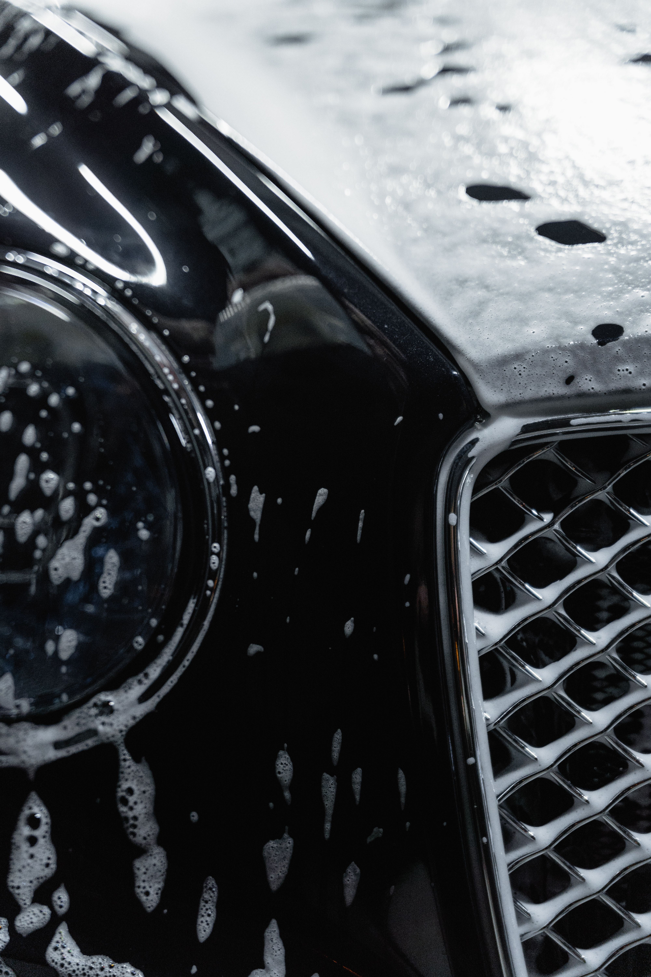 Close-up of an SUV headlight and grille covered in cleaning foam.