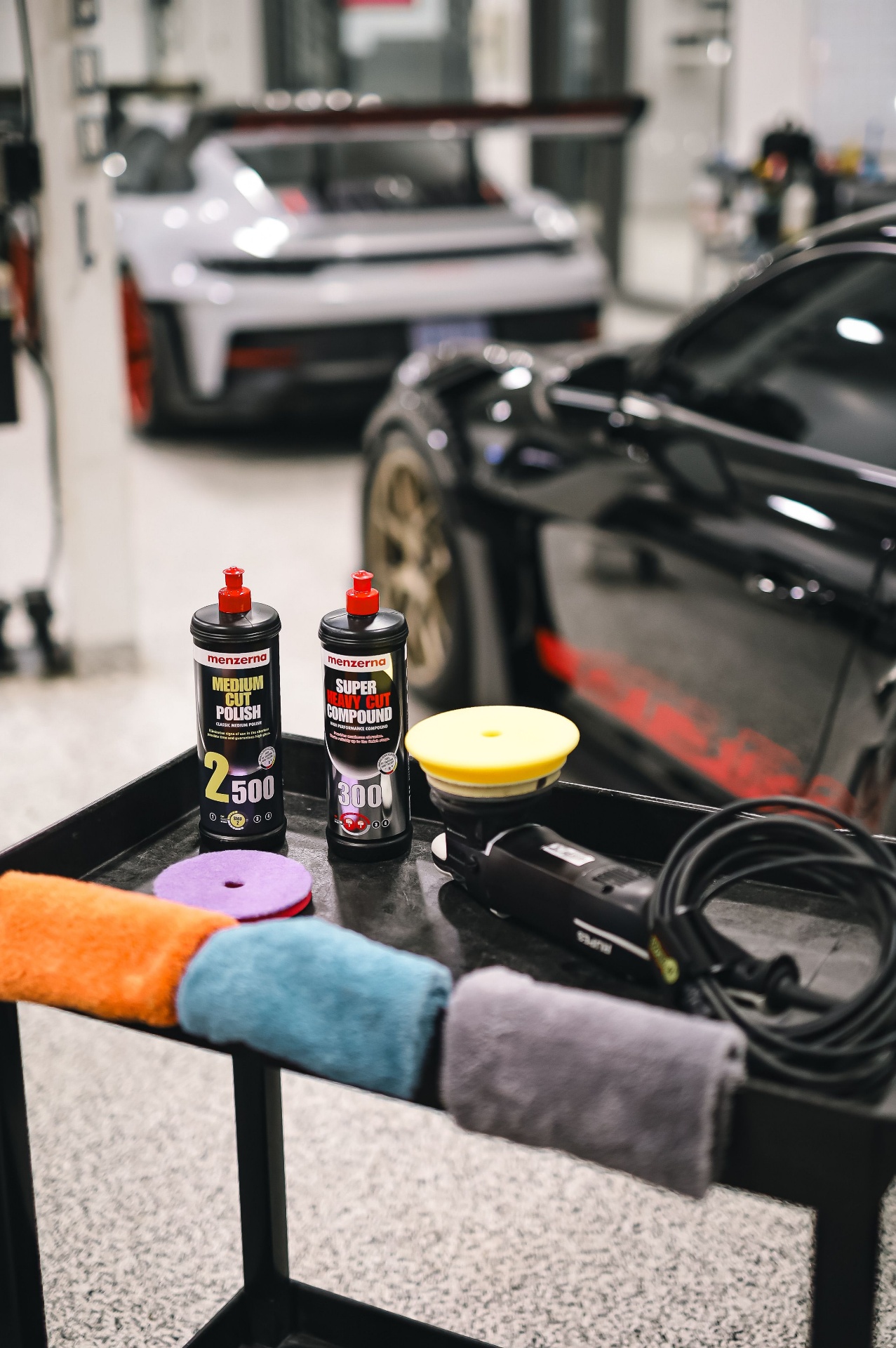 Detailing cart with polish bottles, microfibre towels, and a machine polisher laid out beside a vehicle.